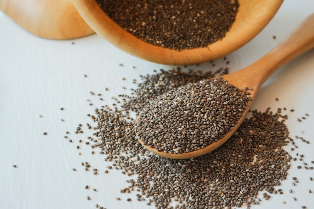 Foto pilha de sementes de chia e colher com tigela de madeira no fundo branco