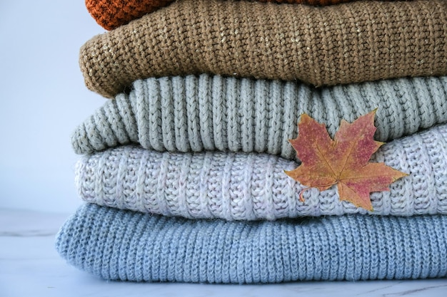 Pilha de suéter quente de malha aconchegante com folhas de bordo de outono Suéteres em estilo retrô cores laranja e azul Conceito de hygge aconchegante Copiar espaço