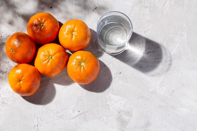 Pilha de tangerinas frescas e vidro com água na mesa de concreto