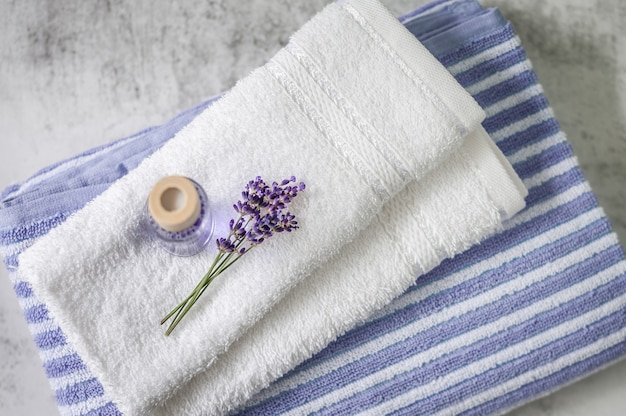 Pilha de toalhas macias limpas com um monte de lavanda e purificador de ar em cinza claro. Toalhas de spa contra uma parede texturizada. Minimalismo, foco suave, vista superior.
