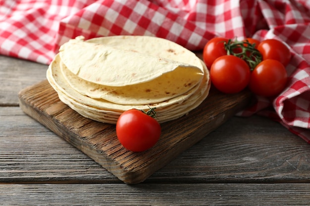 Pilha de tortilha de farinha de trigo integral caseira e legumes na tábua no fundo da mesa de madeira