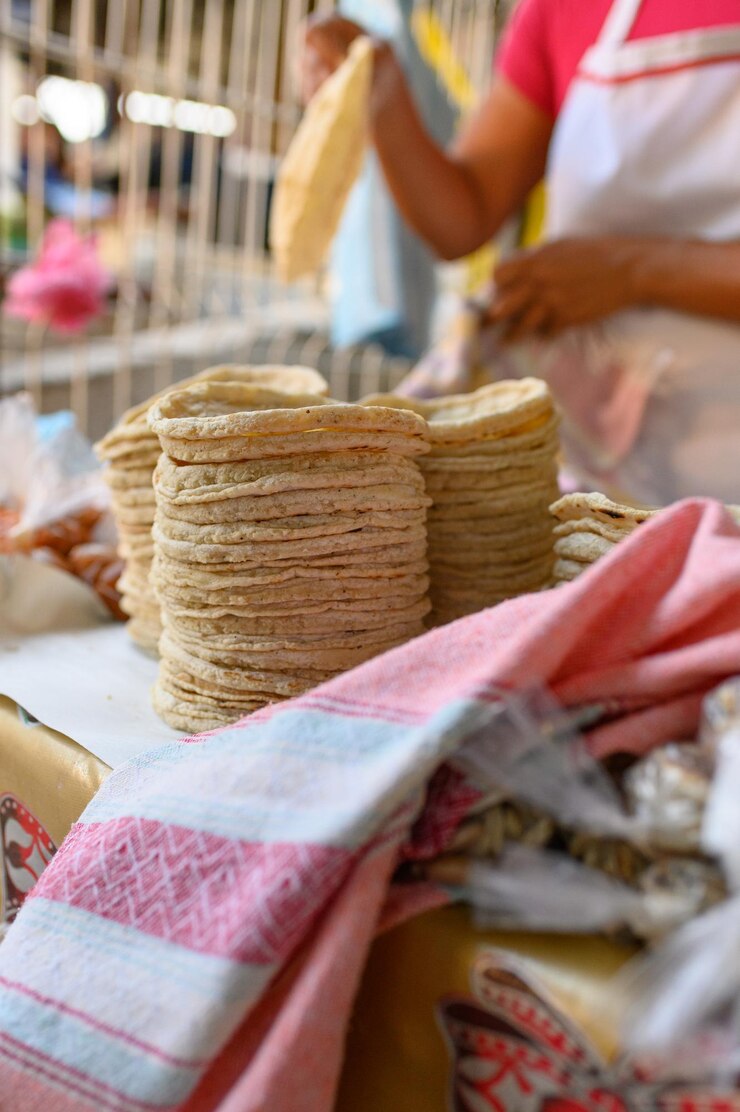 Foto pilha de tortilhas recém-feitas no balcão perto de uma cozinheira anônima trabalhando em uma barraca no mercado local durante o dia