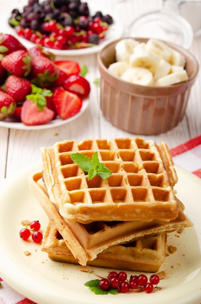 Pilha de três waffles belgas na mesa de cozinha branca com morangos bananas e groselha