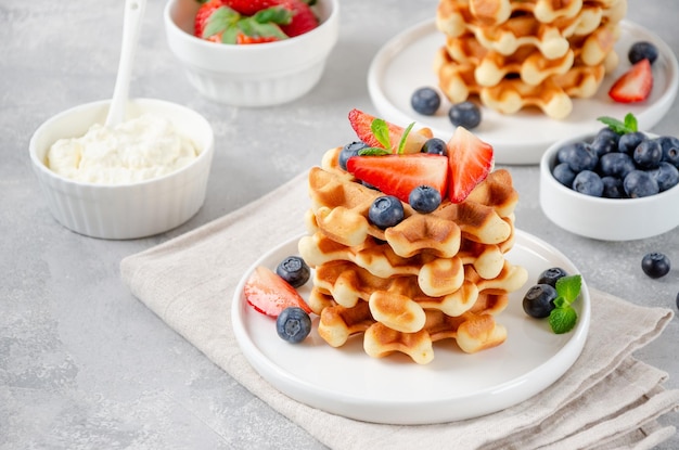 Pilha de waffles belgas com morangos frescos mirtilos e creme na chapa branca Copie o espaço