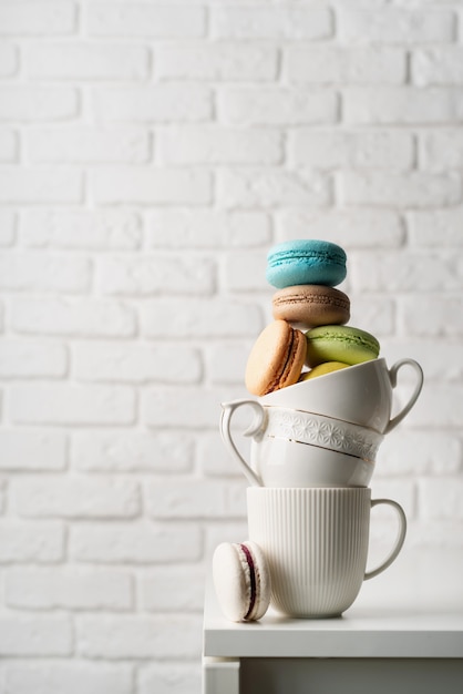 Pilha de xícaras de café brancas cheias de biscoitos na borda da mesa, fundo de parede de tijolo branco