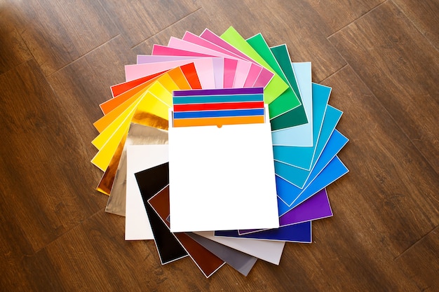 Foto pilha retorcida de folhas coloridas 12x12 de papel adesivo com caixa isolada sobre o fundo marrom. brincar. cores sortidas.