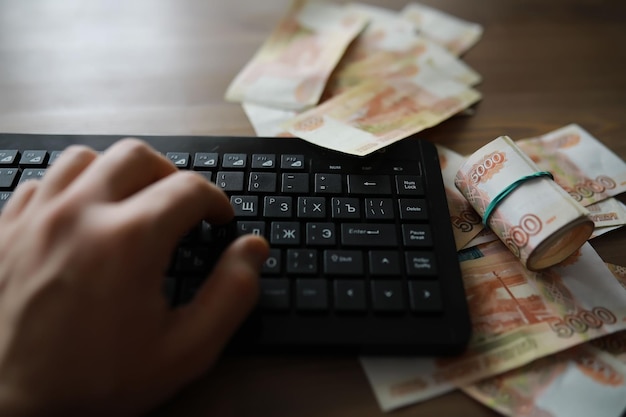 Pilhas de notas de 5000 rublos na mesa ao lado do laptop Poupança e investimentos nas condições de sanções e inflação