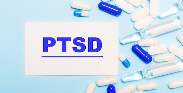 Pillen, Ampullen und eine weiße Karte mit dem Text PTBS auf einem hellblauen Tisch. Medizinisches Konzept