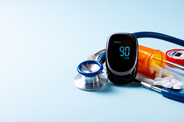 Pillen in der orange Flasche mit Blutzuckermessgerät und Stethoskop auf blauem Hintergrund