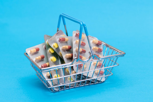 Pillen und Kapseln im Warenkorb auf blauem Hintergrund