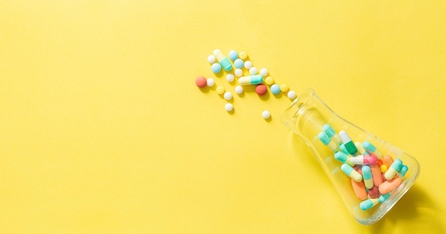 Pillen und Pillenflaschen auf gelbem HintergrundMehrfarbige Tabletten und Pillenkapseln aus Glasflasche