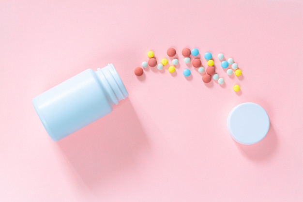 Pillen und Pillenflaschen auf rosa HintergrundRunde Pillen von weißer und orangefarbener Farbe gegossen
