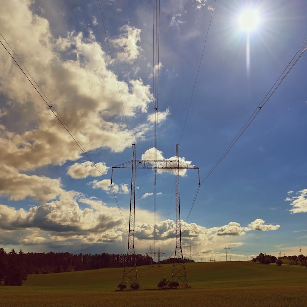 Pilões de alta tensão Céu azul com nuvens e sol na natureza Conceito para tecnologia e indústria