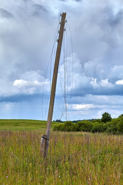 Pilón eléctrico de madera en el campo de verano, los cables sin energía están rotos y colgando en el aire, corte de energía.
