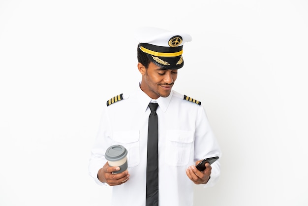Piloto de avión afroamericano sobre fondo blanco aislado sosteniendo café para llevar y un móvil