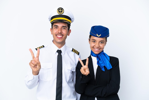 Piloto de avión y azafata de raza mixta aislado sobre fondo blanco sonriendo y mostrando el signo de la victoria