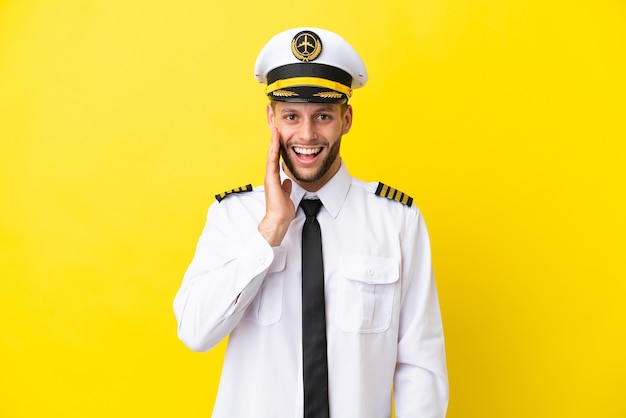 Piloto de avión caucásico aislado sobre fondo amarillo con sorpresa y expresión facial conmocionada