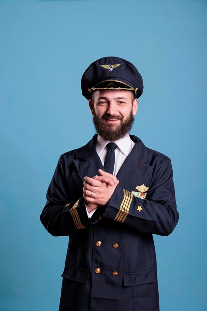 Piloto de avión emocionado sonriente con uniforme profesional aplaudiendo. Feliz capitán de avión positivo aplaudiendo, sacudiendo las palmas, de pie, mirando a la cámara, plano medio del estudio