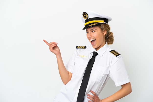 Piloto de avión mujer rubia aislado sobre fondo blanco apuntando con el dedo hacia el lado y presentando un producto