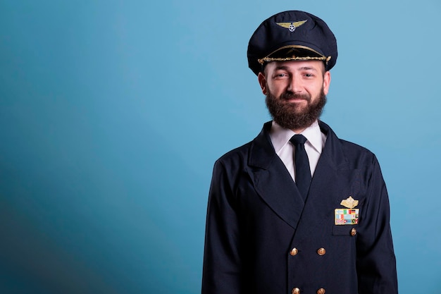 Piloto de avión sonriente con uniforme y retrato de vista frontal de sombrero, capitán de avión mirando a la cámara. Aviador con insignia en chaqueta profesional, miembro de la tripulación de fondo azul