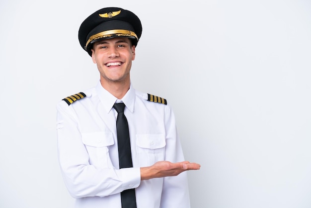 Piloto caucasiano de avião isolado em fundo branco apresentando uma ideia enquanto olha sorrindo para