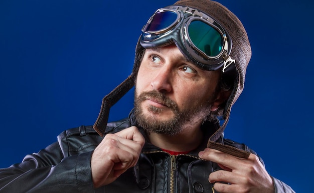 Foto piloto cavalheiro dos anos 20 com óculos escuros e capacete de aviador vintage. usa jaqueta de couro, barba e rostos expressivos