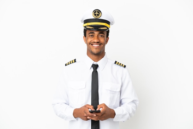 Piloto de avião afro-americano sobre fundo branco isolado enviando uma mensagem com o celular