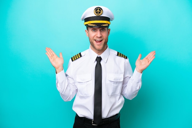 Piloto de avião caucasiano isolado em fundo azul com expressão facial chocada