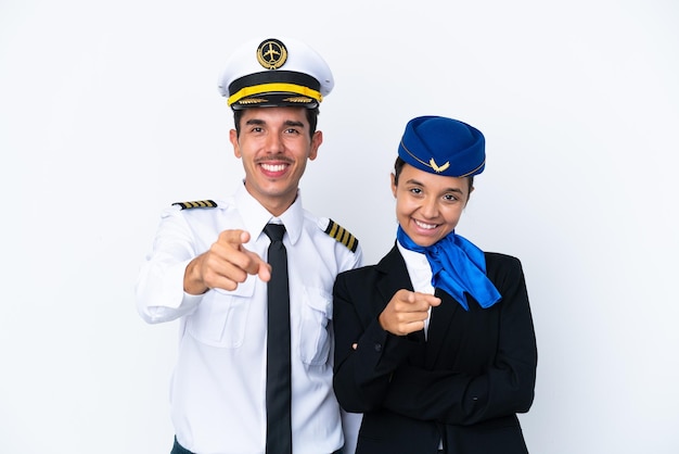 Piloto de avião e aeromoça de raça mista isolada no fundo branco aponta o dedo para você com uma expressão confiante