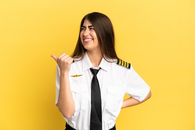 Piloto de avião isolado em fundo amarelo apontando para a lateral para apresentar um produto