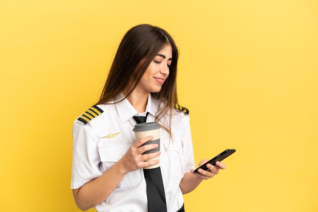 Piloto de avião isolado em fundo amarelo segurando café para levar e um celular
