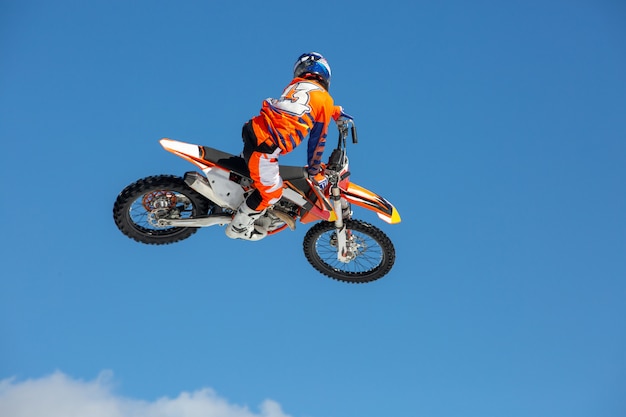 Piloto de moto em voo, pula e decola em um trampolim contra o céu azul