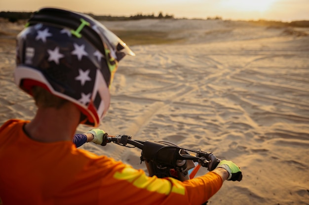 Piloto de motocross MX usando capacete protetor na motocicleta olhando para a estrada de areia. Vista de ombro