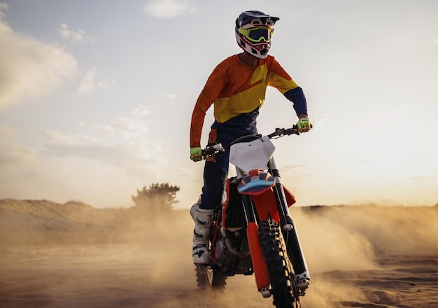 Piloto de motocross usando capacete protetor e terno em moto esportiva no deserto