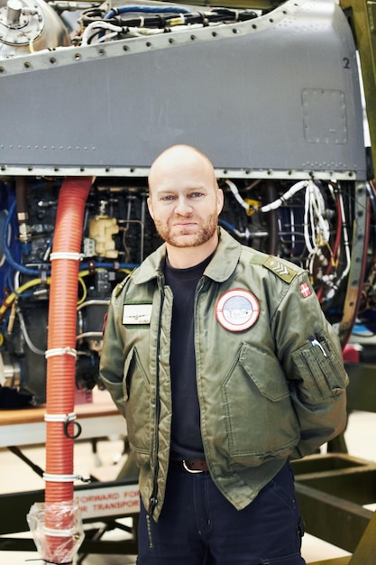 Piloto de retrato e motor militar ou engenheiro de aeronaves masculino de uniforme e avião no hangar Manutenção de aviões e equipamento de oficial ou mecânico de homem em aeronaves dianteiras para reparos ou exército e asfalto