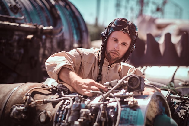 El piloto diligente está trabajando en el motor del avión. Lleva uniforme y casco. Es un día muy sanny afuera.