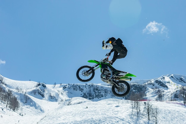 Piloto em uma motocicleta em vôo salta e decola em um trampolim contra as montanhas nevadas Conceito ativo extremo raio de luz