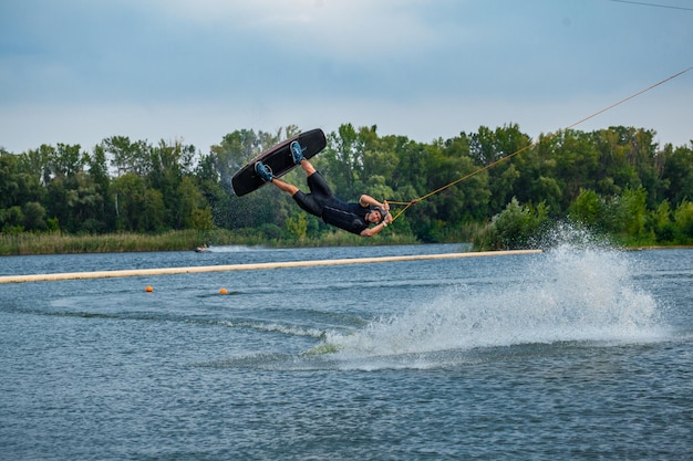 Piloto experimentado de wakeboard saltando y girando en el aire sujetando el cable de remolque