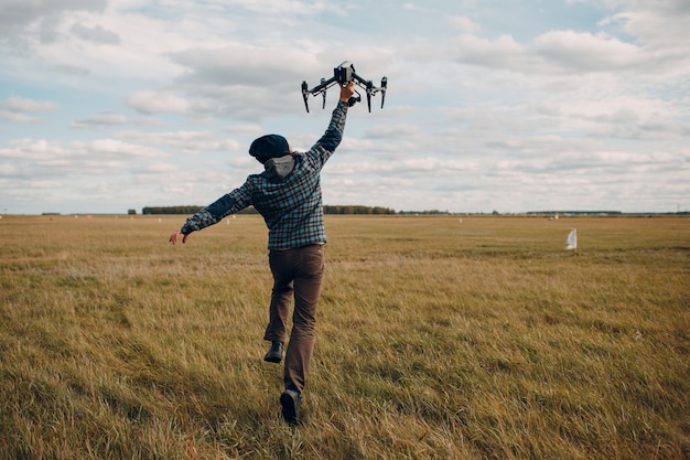 Piloto de hombre sosteniendo drone quadcopter en manos en el campo exterior.