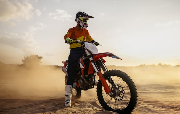 Piloto de motocross con casco protector y traje en moto deportiva sobre paisaje de polvo