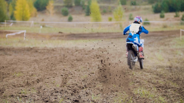 Piloto de motocross comienza a andar en su motocicleta dirt Cross MX: vista trasera, telefoto