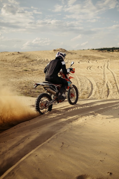 Piloto de motocross conduciendo sobre una duna de arena más abajo en una pista todoterreno que sopla polvo debajo de la rueda