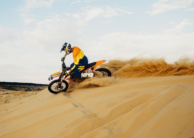 Piloto de motocross profesional con casco y traje protector deslizándose por la colina de arena. Carreras de motos de velocidad