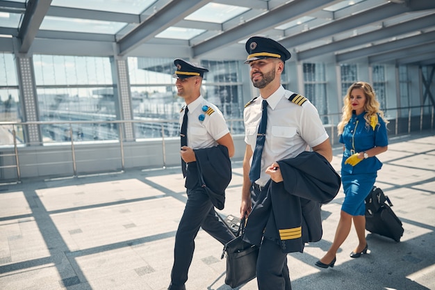 Pilotos masculinos guapos y azafata encantadora con bolsas de viaje y sonriendo