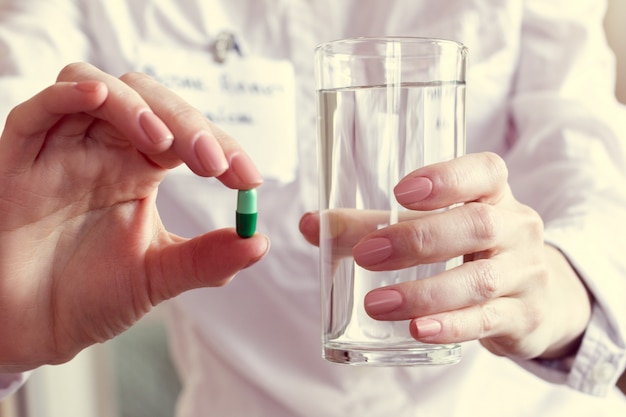 Pílula e um copo de água nas mãos de um médico