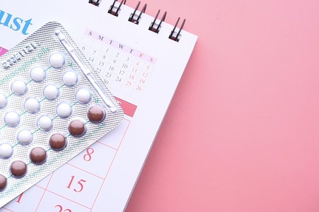 pílulas anticoncepcionais, calendário e bloco de notas na mesa