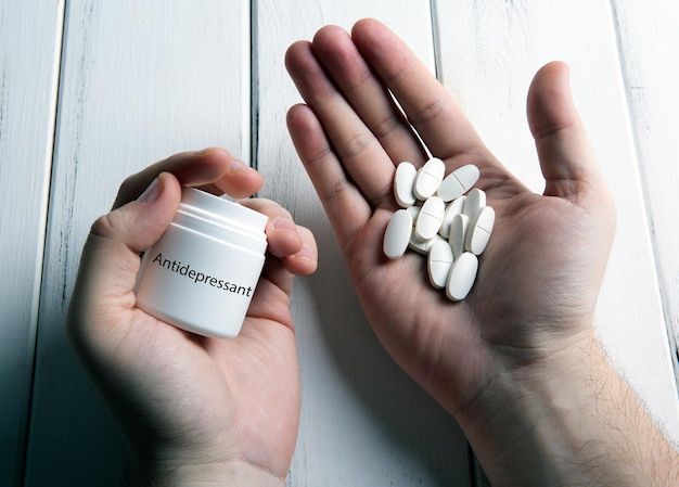 Foto pílulas brancas e uma jarra com antidepressivo de inscrição na mão humana em uma mesa de madeira