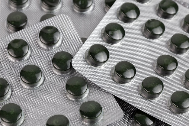 Pílulas de espirulina verde idênticas em blisters médicos em close-up com foco seletivo e desfocamento