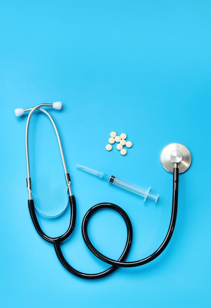 Pílulas de estetoscópio e seringa em fundo azul vista superior conceito de cardiologia e cuidados de saúde