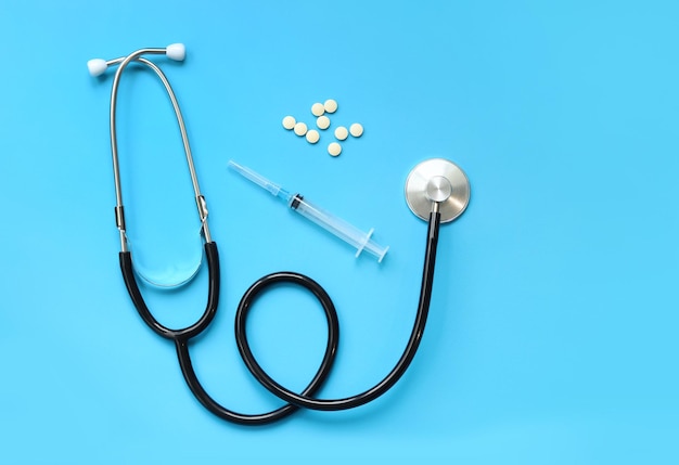Pílulas de estetoscópio e seringa em fundo azul vista superior conceito de cardiologia e cuidados de saúde